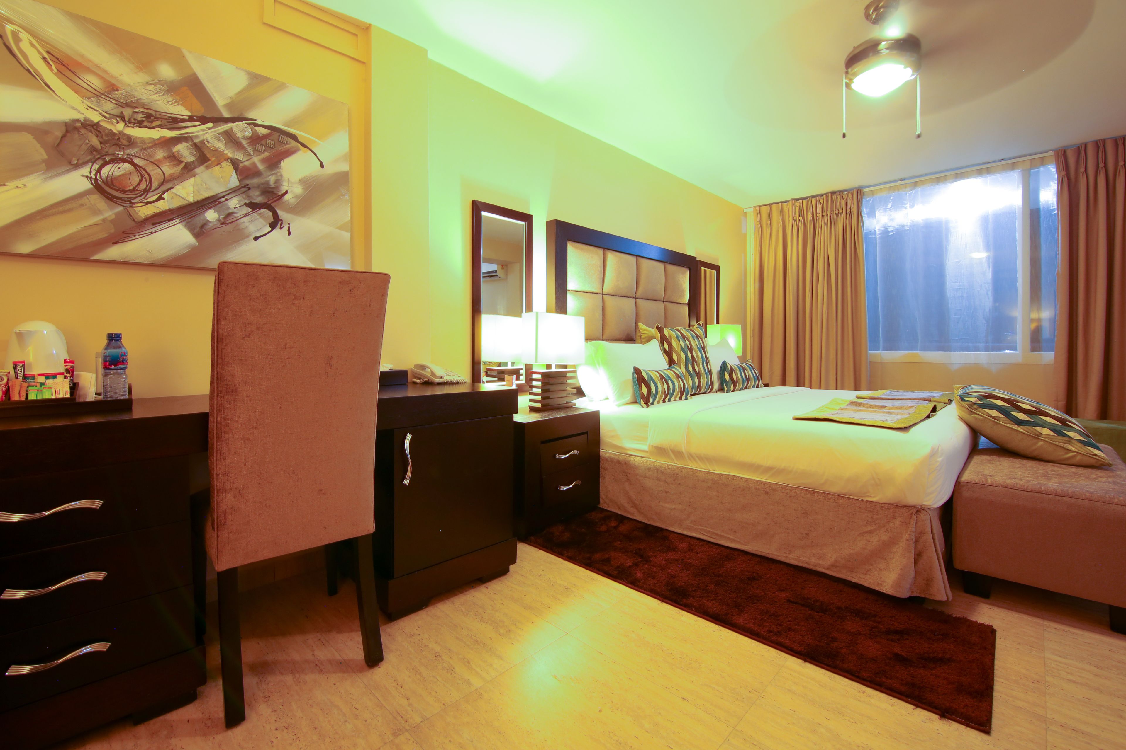 A hotel room with a bed, bedside table, lamp, and a painting on the wall.