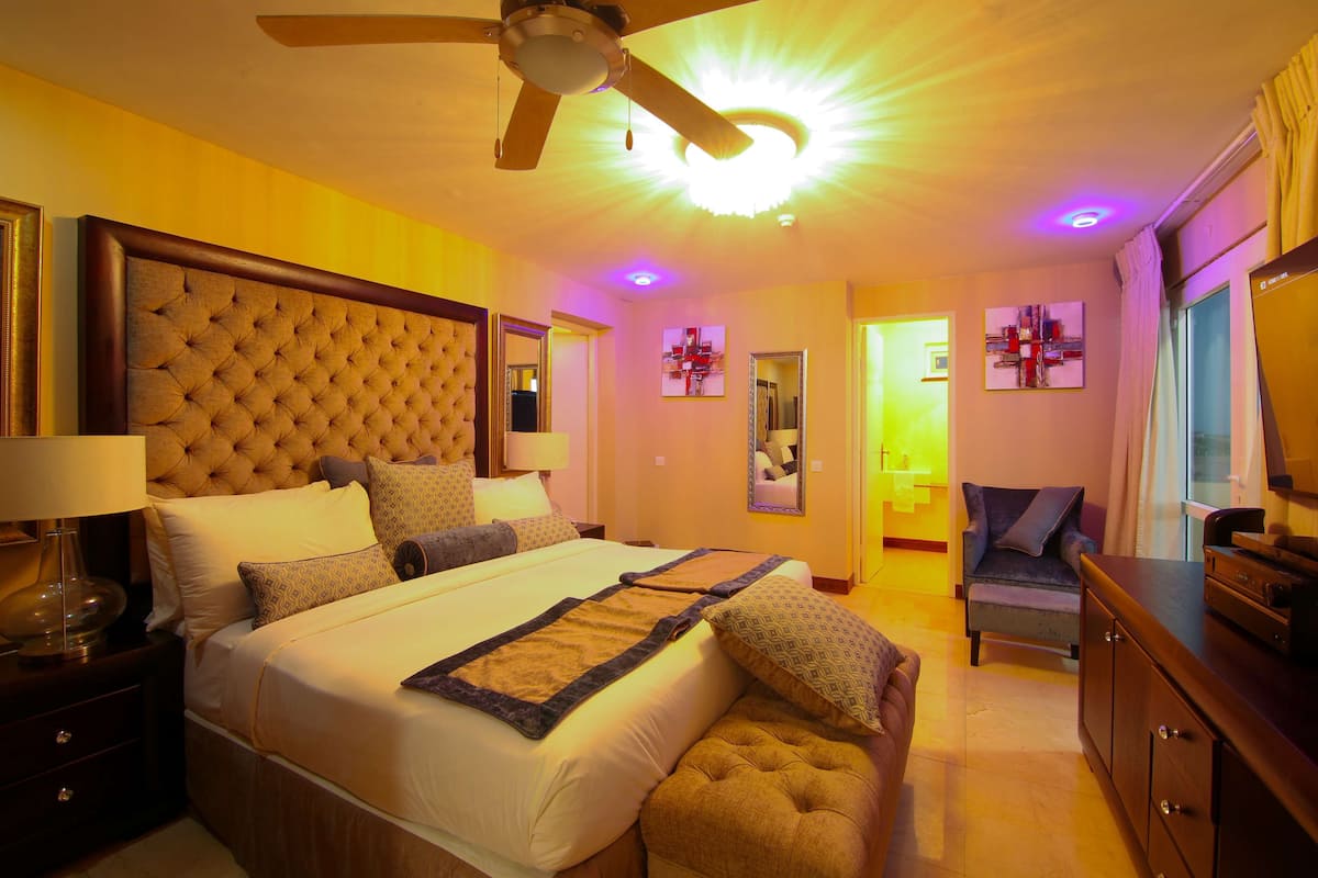 A well-lit bedroom with a large bed, a ceiling fan, and a TV on a wooden cabinet.