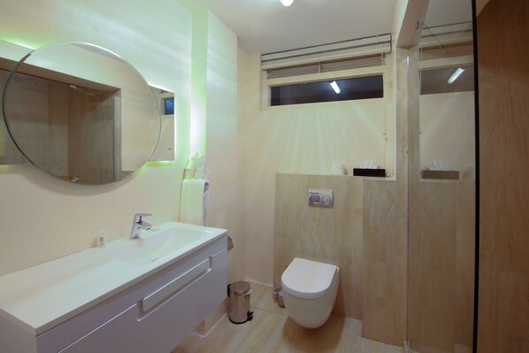 Un baño moderno con tocador blanco, un espejo redondo, un inodoro y una zona de ducha.