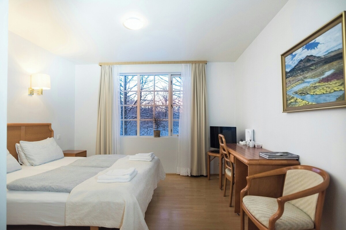 A hotel room with a bed, a desk, a chair, a television, and a painting on the wall.