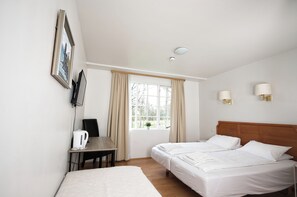 A hotel room with a bed, a desk with a kettle, a chair, a window with curtains, and a wall-mounted TV. - Hotel Laxnes (Mosfellsbær)