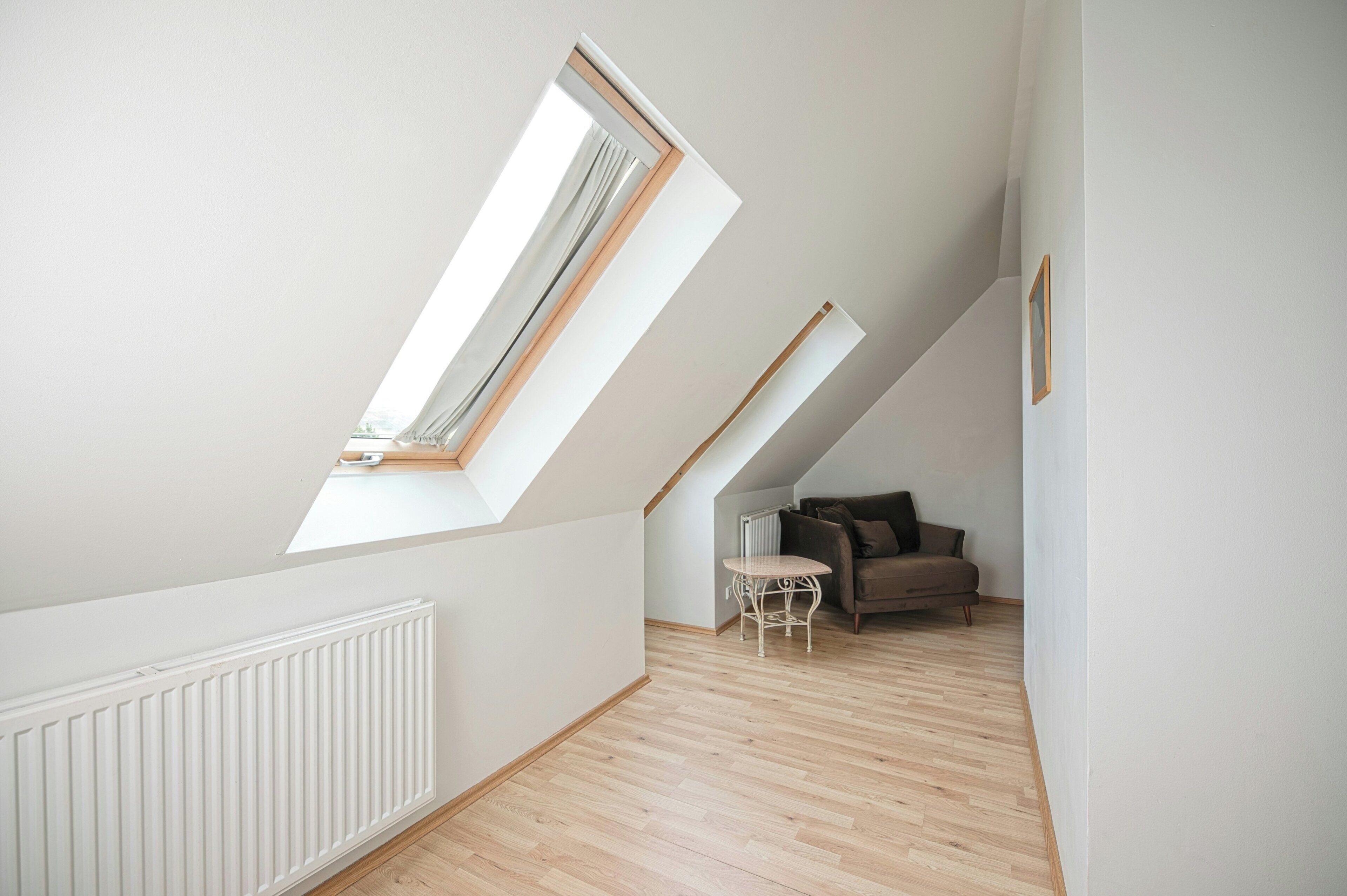 A room with sloped ceilings, a radiator, a wooden floor, a small table, and a sofa.