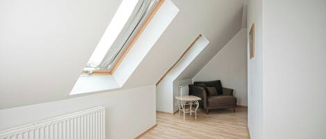 A room with sloped ceilings, a radiator, a wooden floor, a small table, and a sofa.