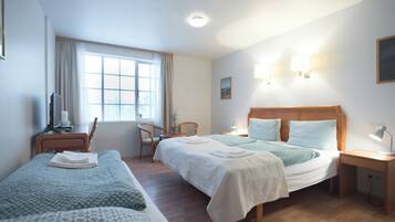 A hotel room with two beds, a desk, a chair, a window, and a wall-mounted lamp.