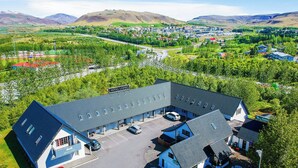 A hotel with a parking lot, a road in the background, and a mountainous landscape. - Hotel Laxnes (Mosfellsbær)