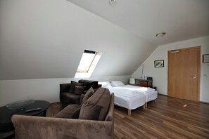 A modern bedroom with a sloped ceiling, a bed with white bedding, a brown sofa, and a small table with a remote control. - Hotel Laxnes (Mosfellsbær)