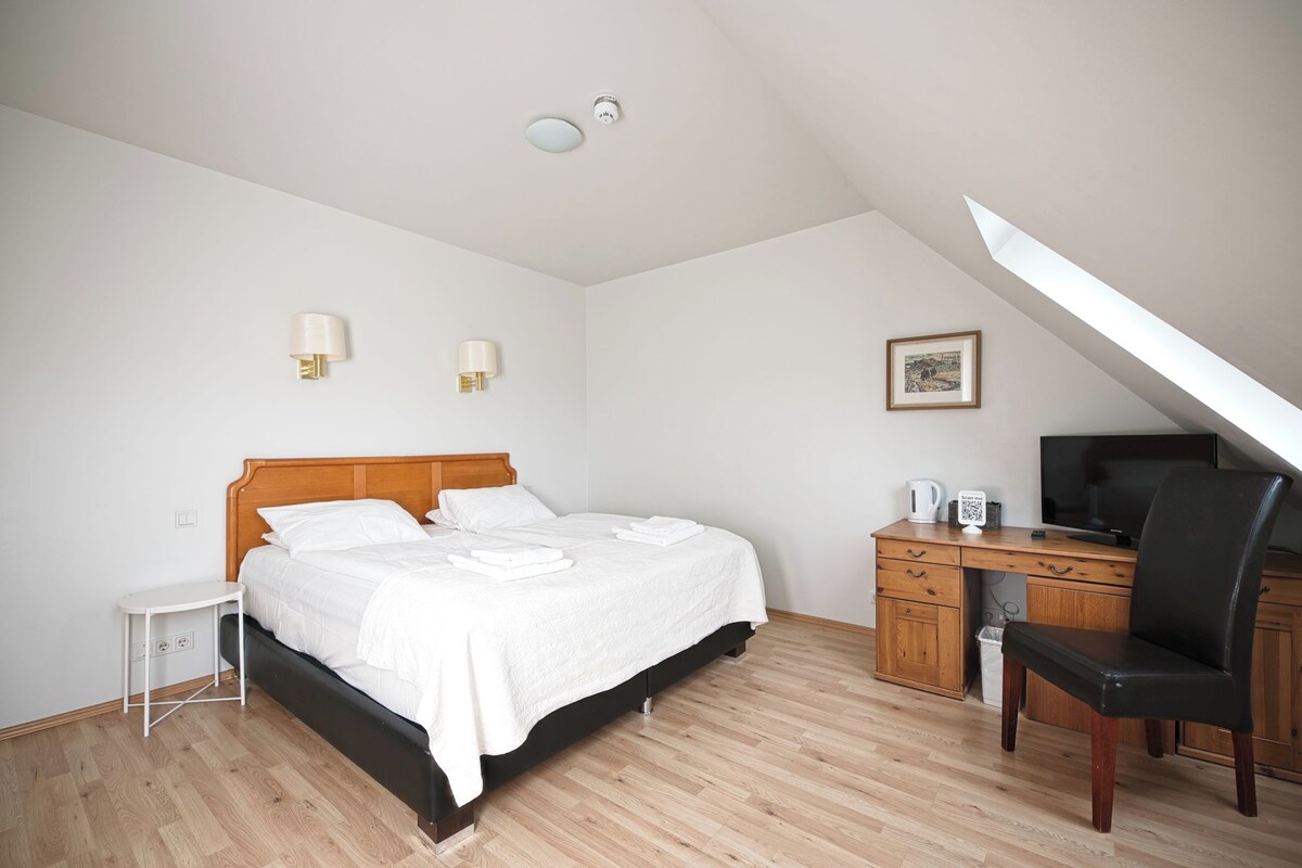 A bedroom with a bed, bedside table, desk, chair, and a television.