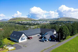 A hotel with a parking lot and a view of a town and hills in the background. - Hotel Laxnes (Mosfellsbær)