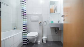 Et moderne badeværelse med et hvidt toilet, en bruser med stribet gardin, en vask med et spejl over og en skraldespand.