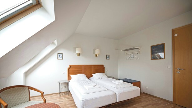 A bedroom with a sloped ceiling, a wooden bed, a bedside table, a chair, and a small table. - Hotel Laxnes (Mosfellsbær)