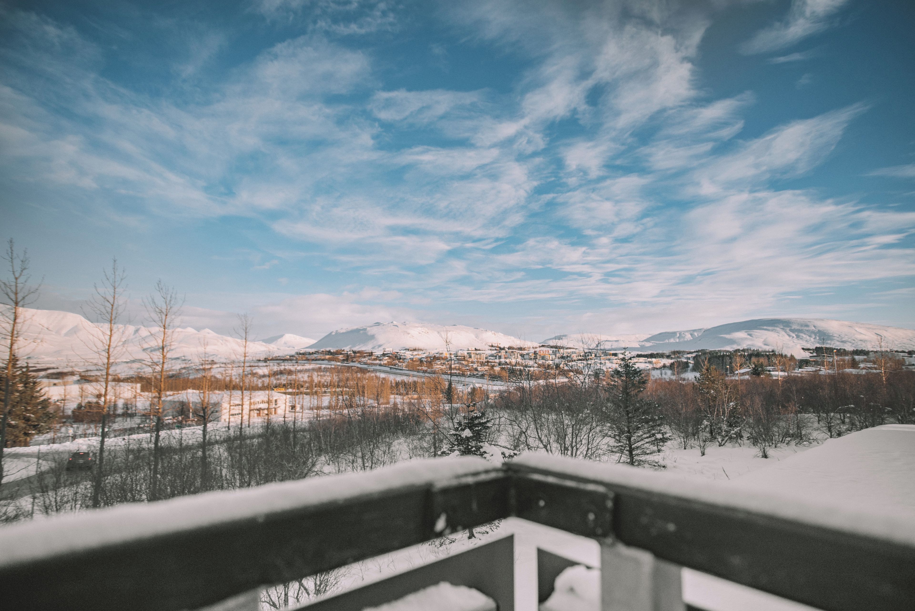 A snowy landscape with a town in the distance, a clear sky, and a snow-covered mountain range.