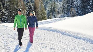 Dos personas caminando por un sendero cubierto de nieve, con árboles al fondo.
