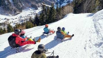 A group of people sledding down a snowy slope with a mountainous backdrop.