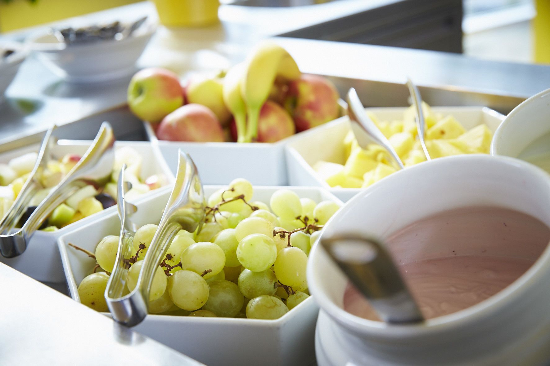 Un bufé con diversas frutas y un tazón de postre rosado.