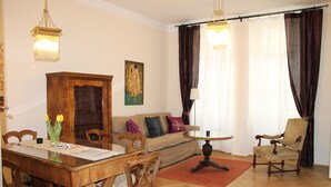 A living room with a wooden dining table, chairs, a sofa, a patterned armchair, and a painting on the wall. - Appartements Hermine (Vienna)