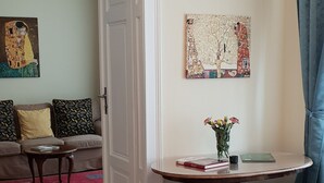 A room with a bed, a desk with a vase of flowers, a painting on the wall, and a door leading to another room. - Appartements Hermine (Vienna)