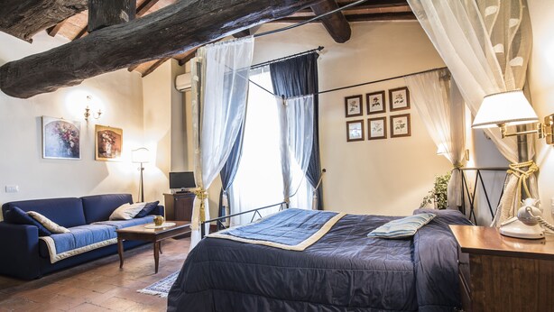 A bedroom with a large bed, a sofa, a desk, and a lamp. - Palazzo Fani Mignanelli (Siena)