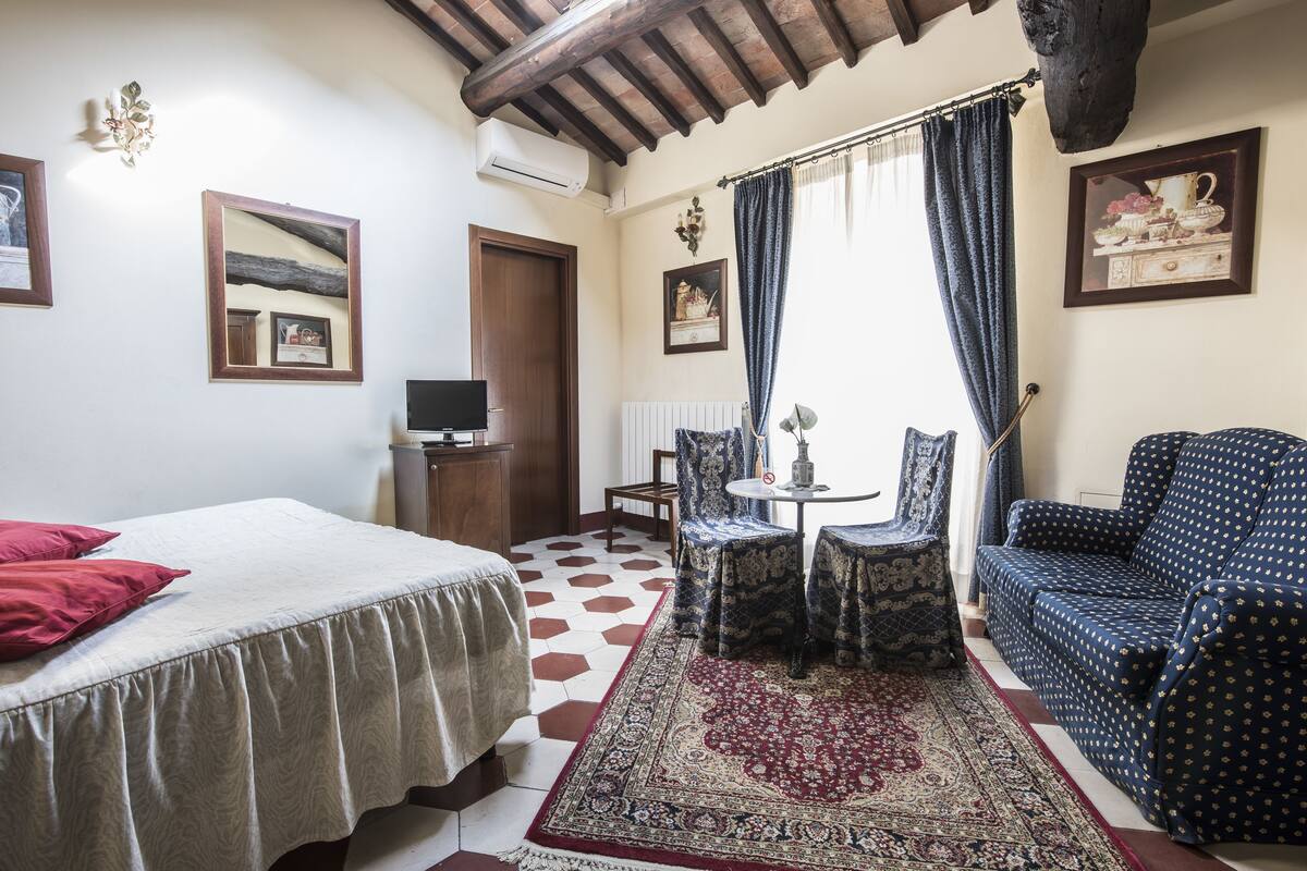 A hotel room with a bed, a sofa, a small table with chairs, a rug, and a TV.