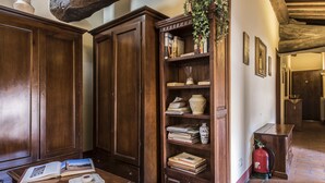 A wooden bookcase with books and decorative items, a wooden table with an open book, and a fire extinguisher on the floor. - Palazzo Fani Mignanelli (Siena)