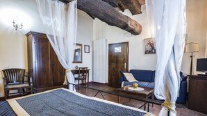 A bedroom with a large bed, a wooden ceiling beam, a nightstand, a chair, a sofa, and a lamp. - Palazzo Fani Mignanelli (Siena)