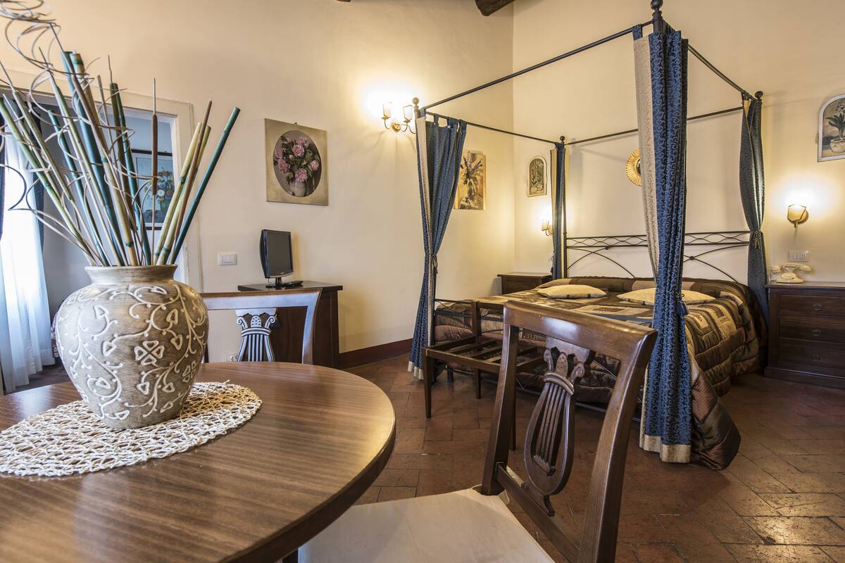 A four-poster bed with a canopy, a wooden dining table with a vase, and a desk with a computer.