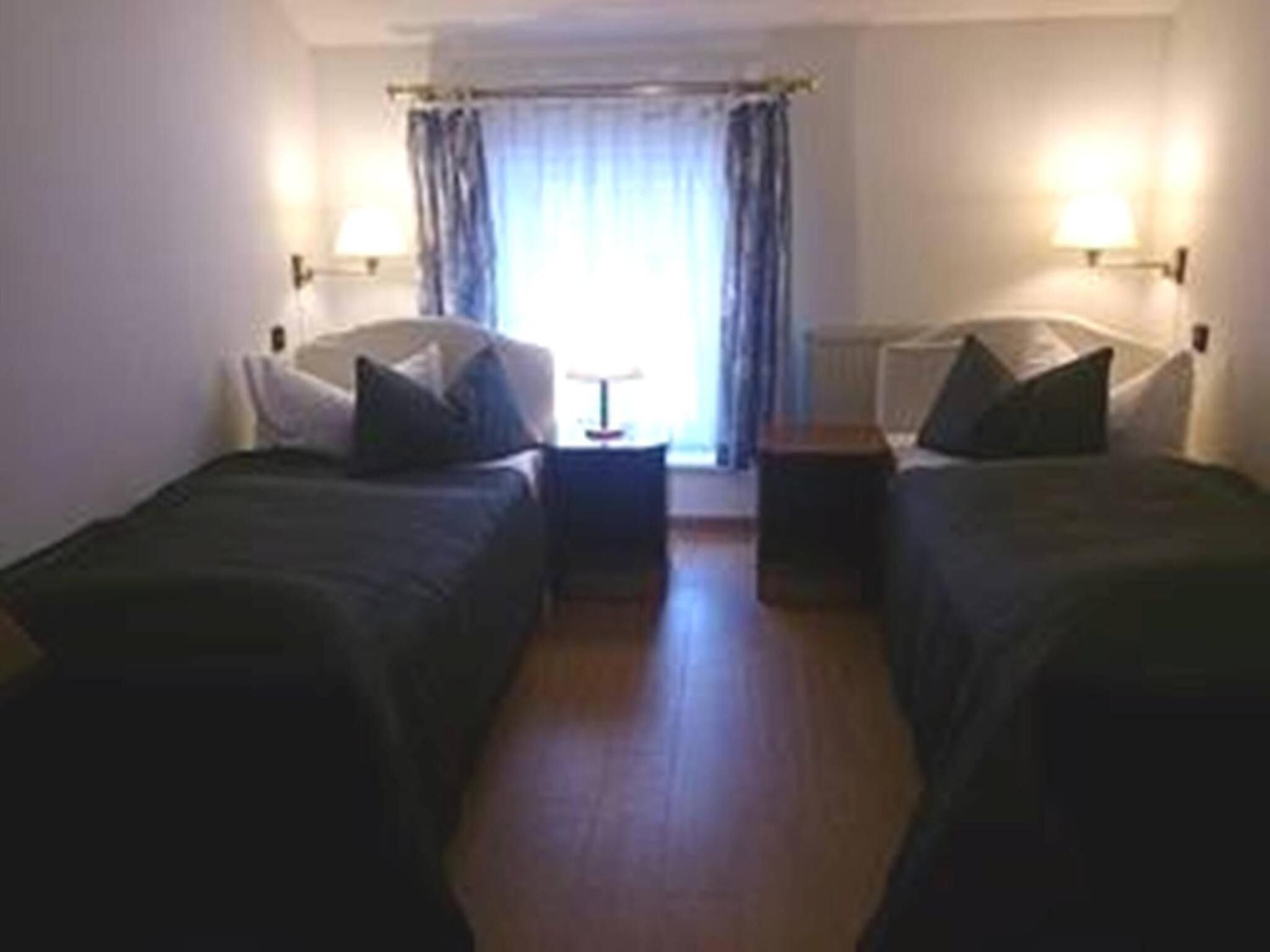 A room with two single beds, a small table, and a lamp.