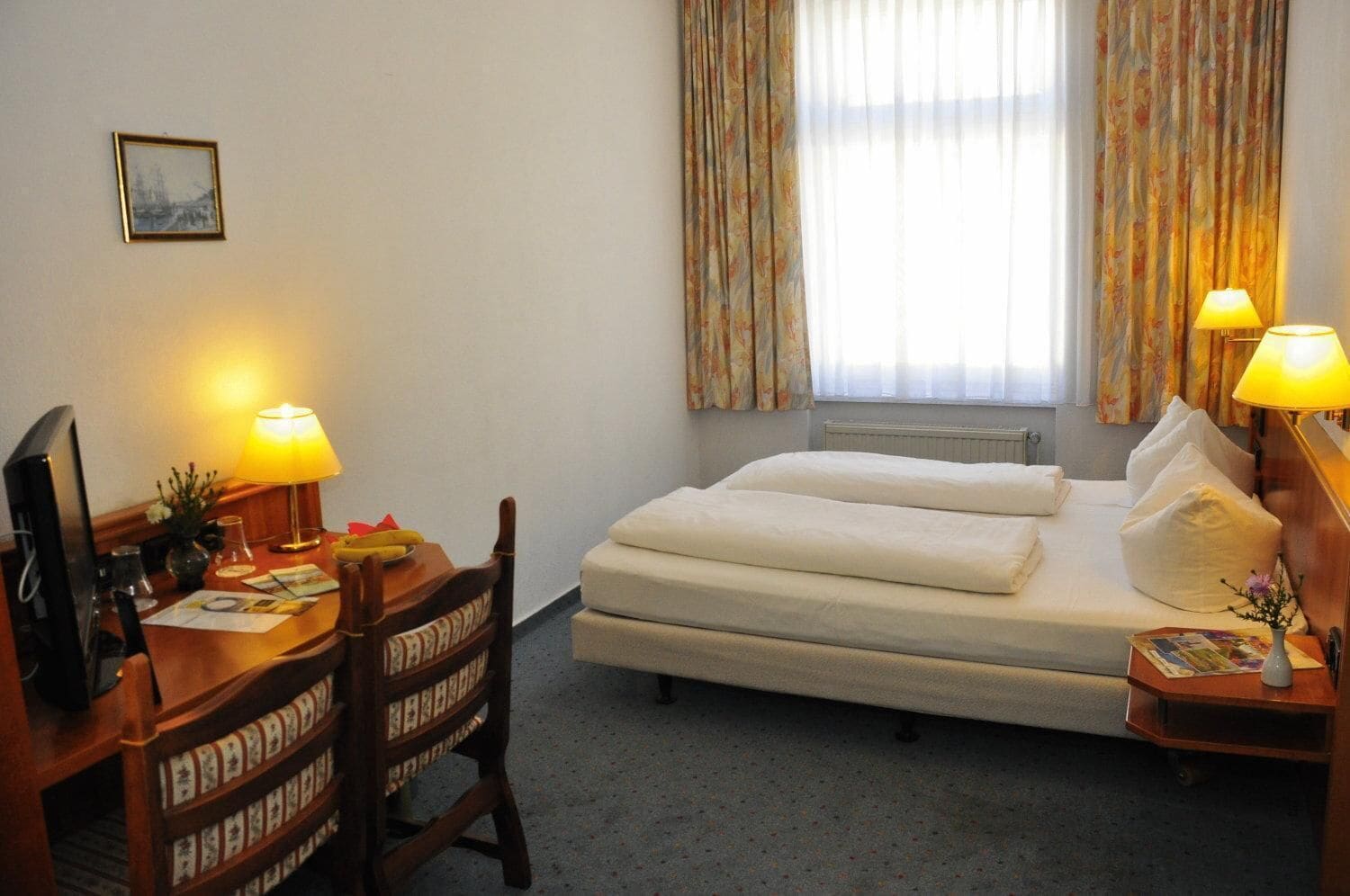 A hotel room with a bed, desk, chair, lamps, and a window with curtains.