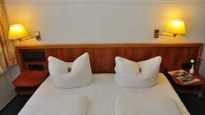 A double bed with white linens, two bedside lamps, a nightstand with a magazine, and a small table with a vase. - Brocki's Hotel Stadt Hamburg (Parchim)