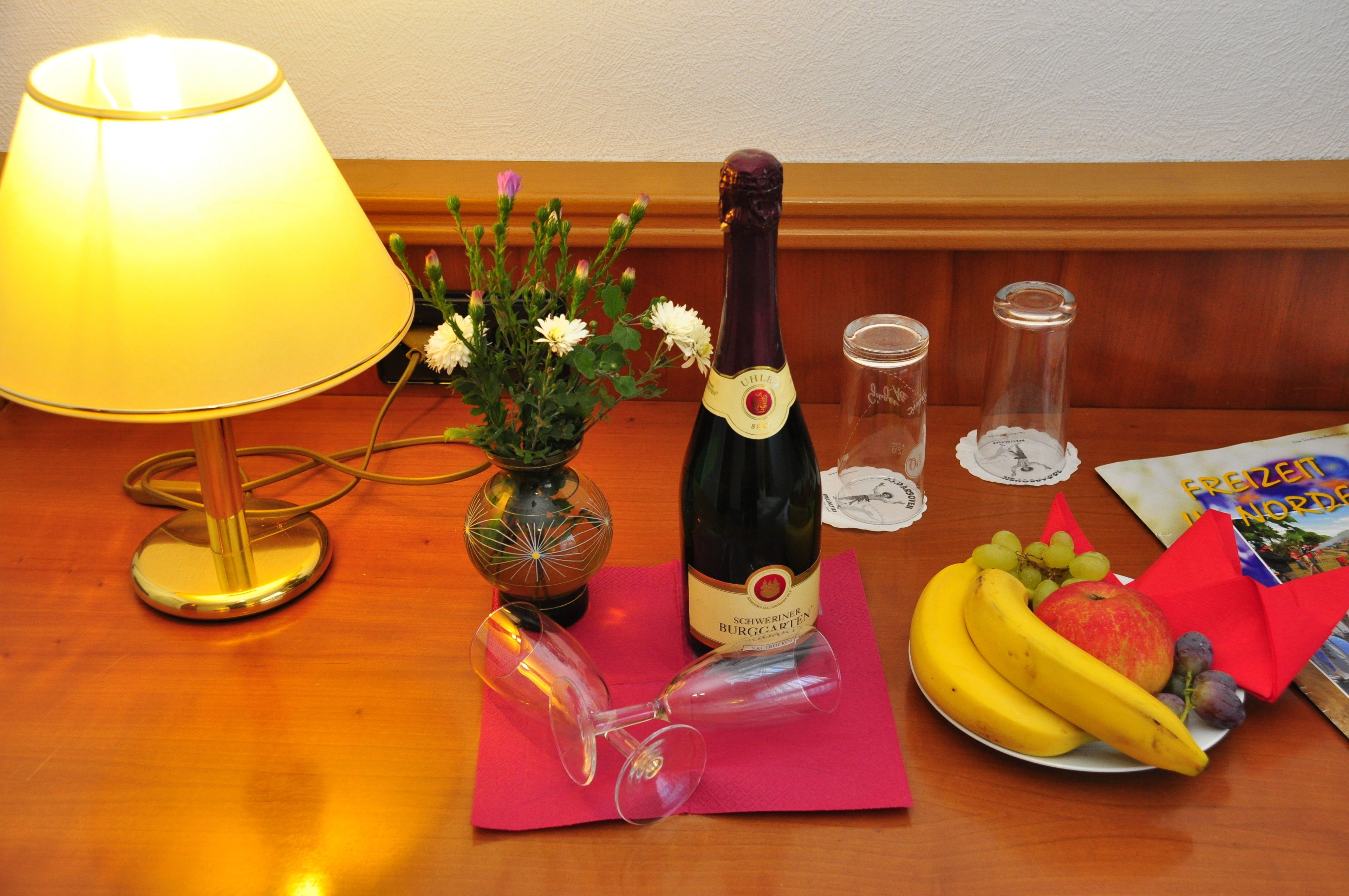 Ein Tisch mit einer Weinflasche, einer Blumenvase, einer Fruchtschale und einer Lampe.