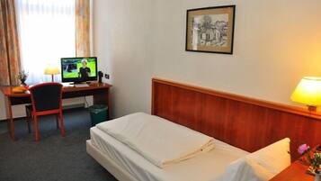A hotel room with a bed, a desk with a computer, a chair, a lamp, and a framed picture on the wall.