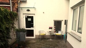 A courtyard with a brick floor, two metal chairs, a potted plant, and a door with a sign. - Brocki's Hotel Stadt Hamburg (Parchim)