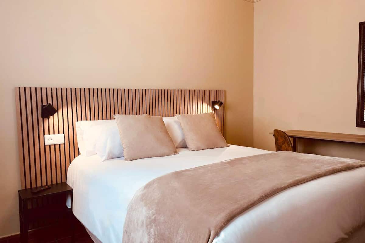A neatly made bed with a wooden headboard, a bedside table, and a wall-mounted light fixture.