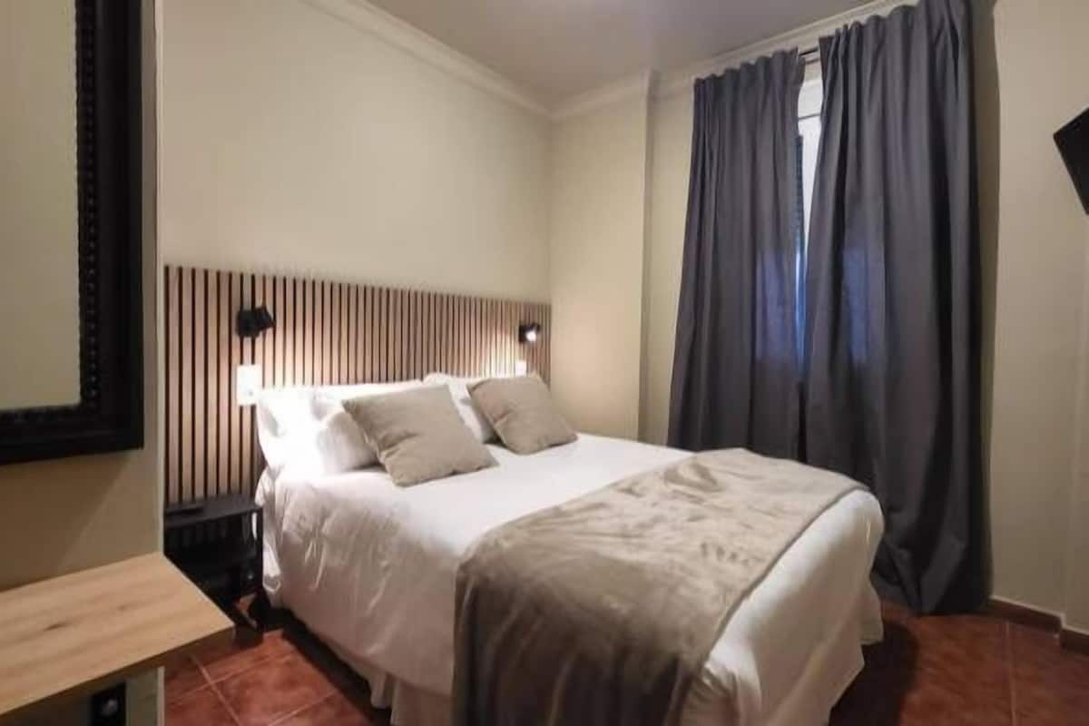 A hotel room with a bed, a bedside table, a mirror, and a TV mounted on the wall.