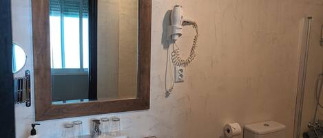 A bathroom with a wooden vanity, a mirror, a sink, a hairdryer, a toilet, and a shower.