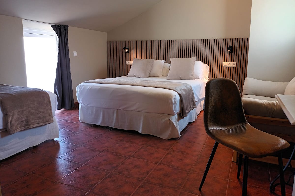 A hotel room with a large bed, a chair, a sofa, and a window with curtains.