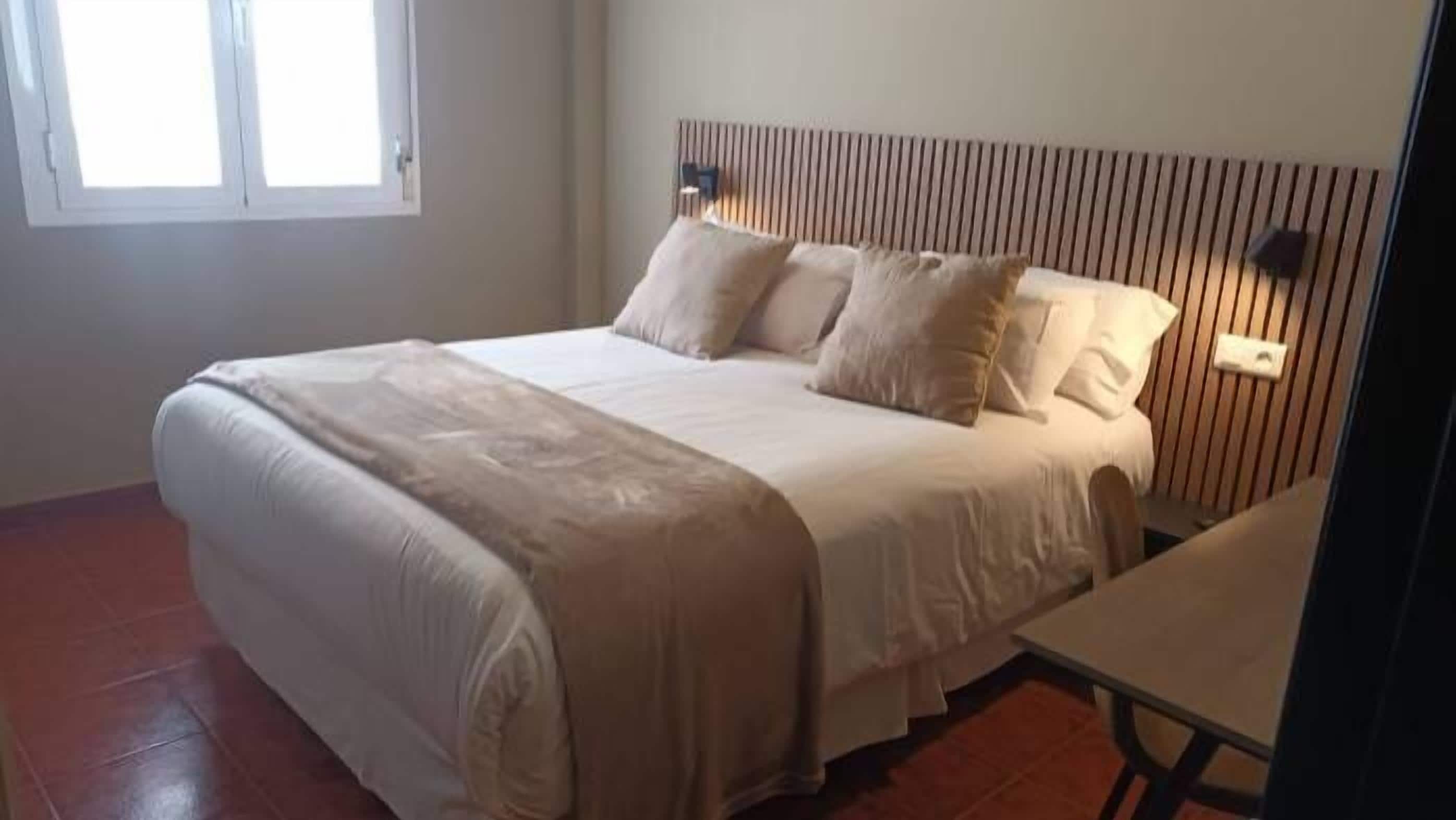Un dormitorio con cama, mesita de noche y ventana.