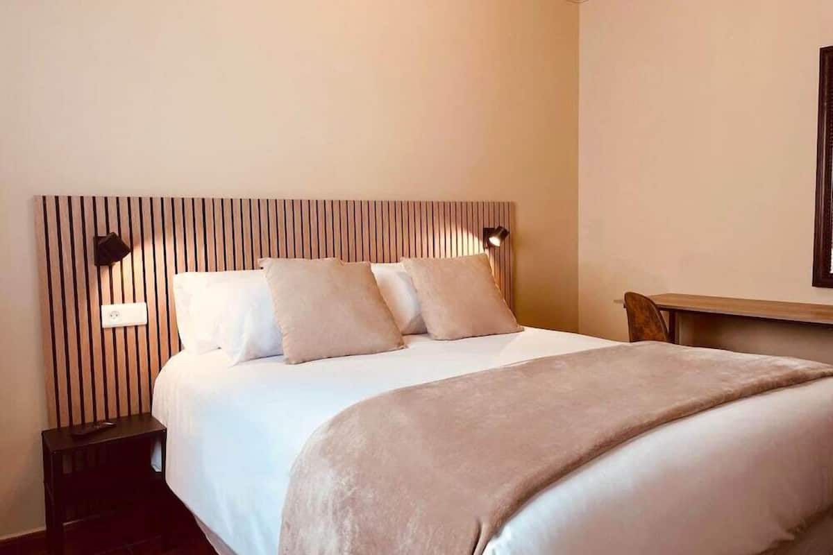 A neatly made bed with a wooden headboard, two bedside tables, and a wall-mounted light fixture.