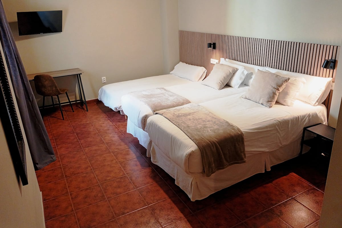 A hotel room with two beds, a desk, a chair, and a TV mounted on the wall.