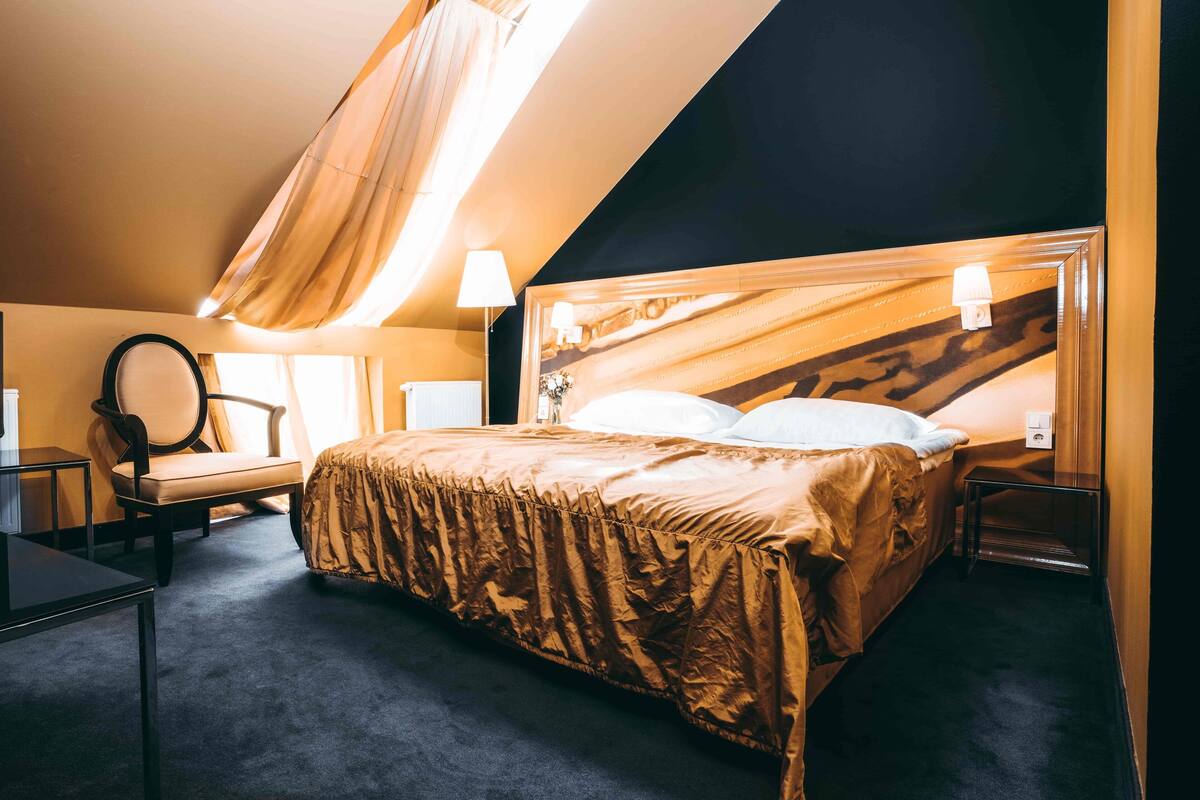 A bedroom with a large bed, a chair, a lamp, and a window with curtains.
