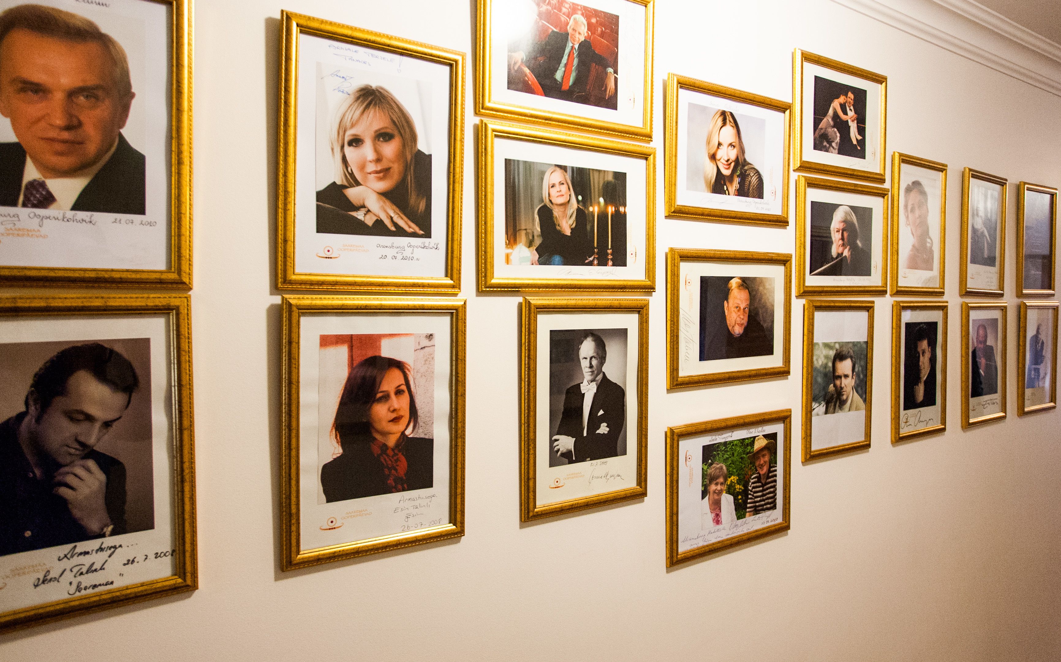 Una pared con múltiples fotografías enmarcadas, cada una con una firma y fecha.