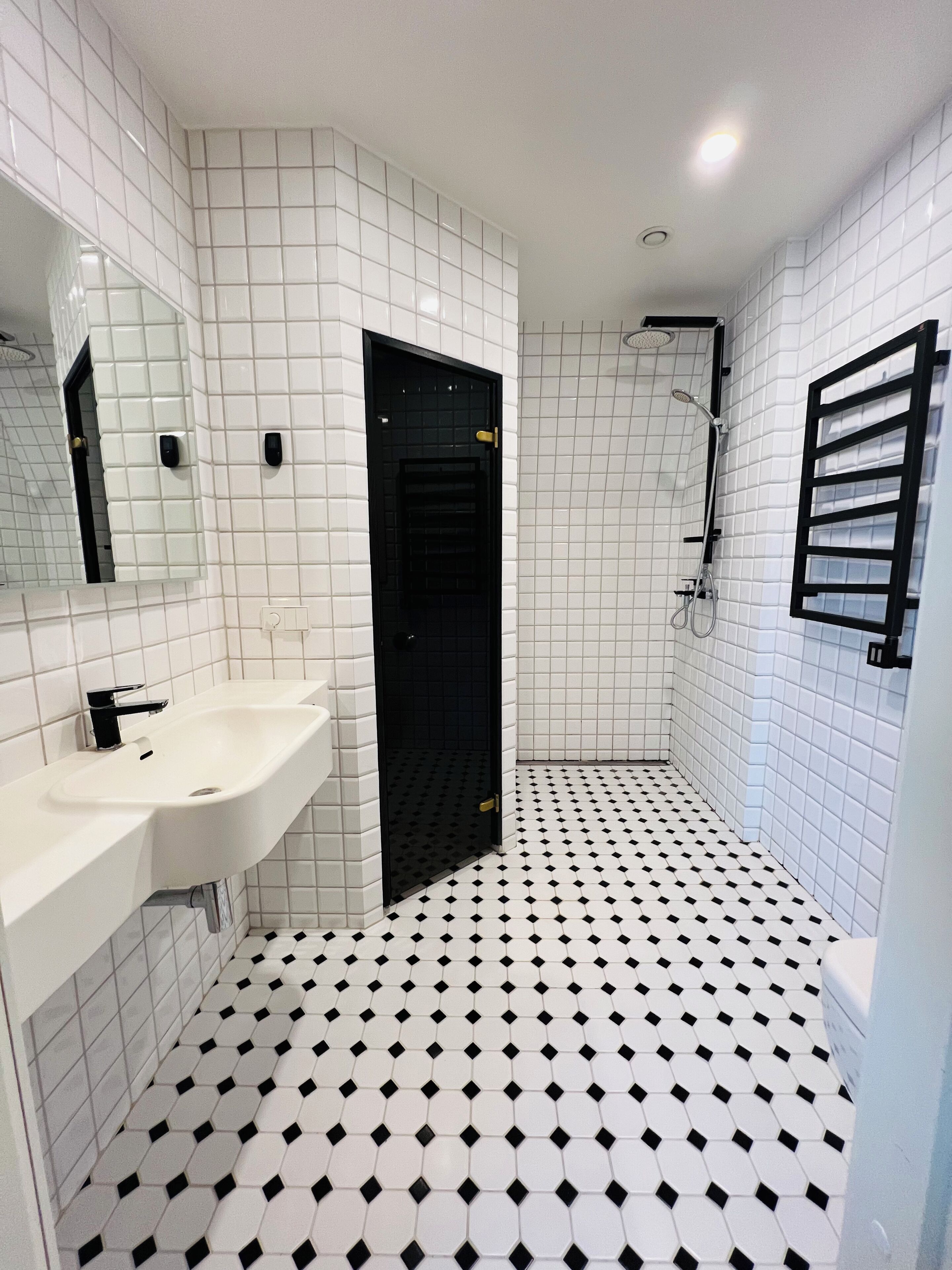Ein Badezimmer mit einem weißen Waschbecken, einer schwarzen Tür und einer Duschkabine.