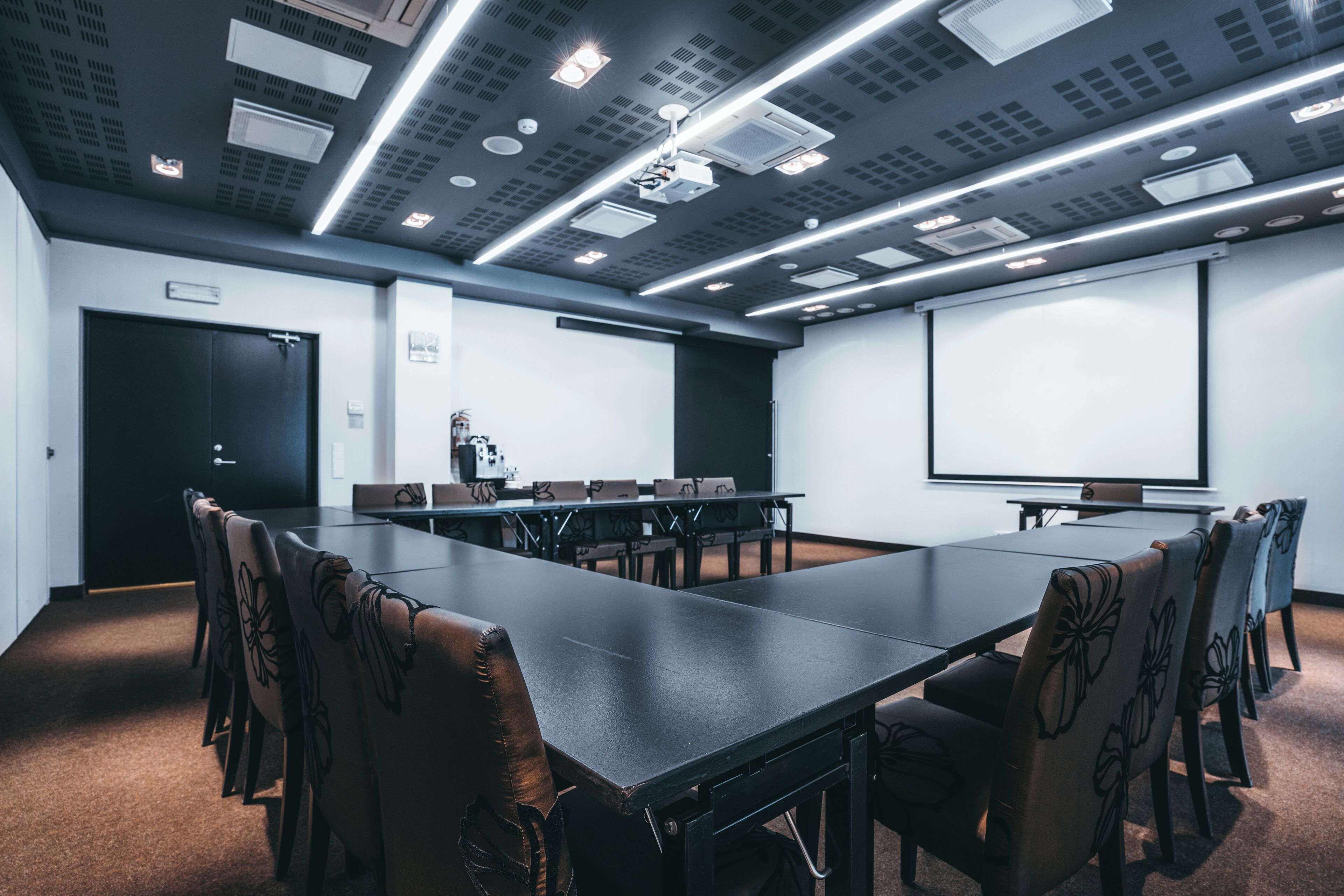 A conference room with a long table, chairs, a projector screen, and a whiteboard.