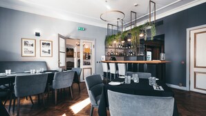 Moderni ravintola, jossa on baarialue, puulattiat ja harmaalla kankaalla verhoillut tuolit.