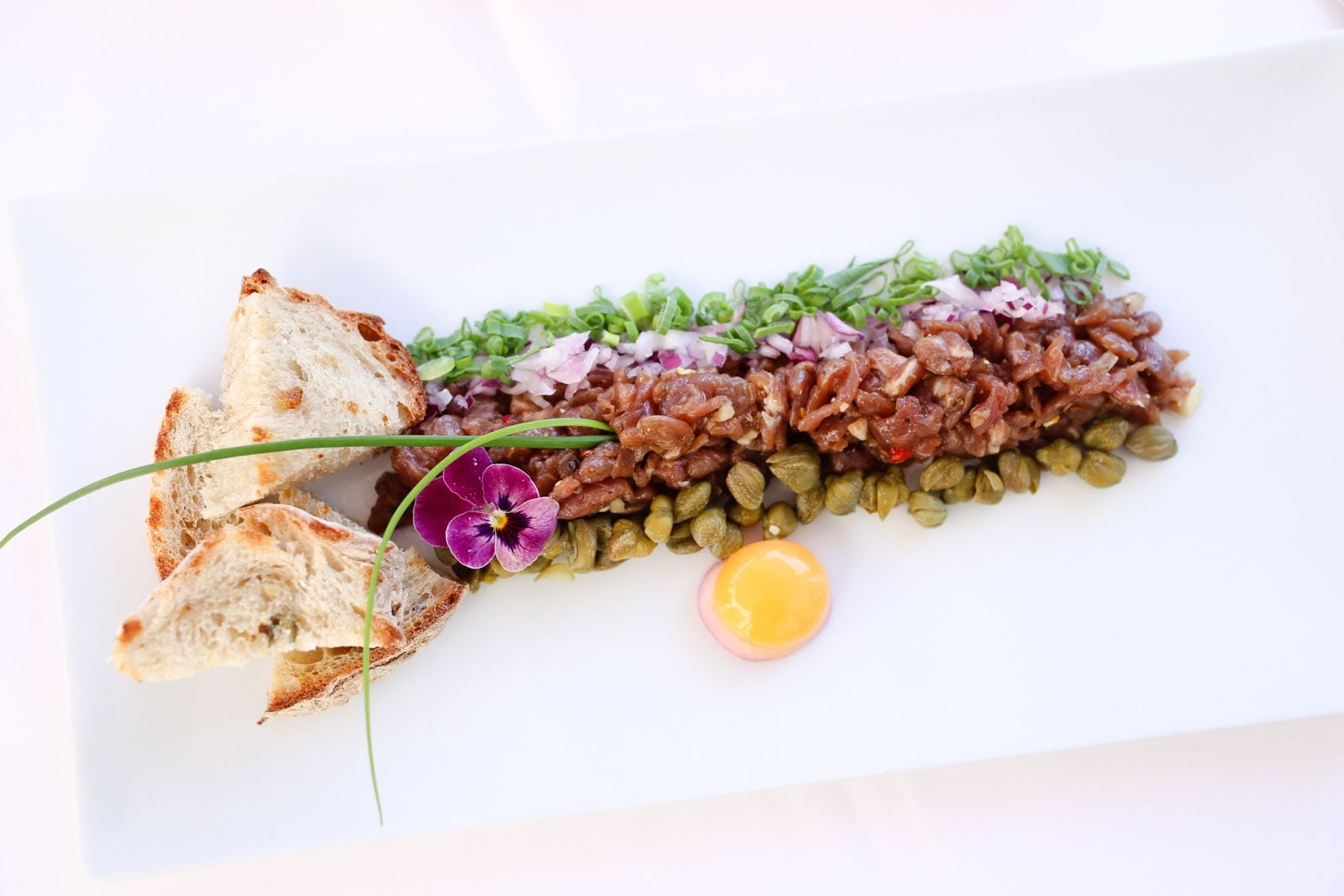 A dish with bread, a flower, and a lemon slice on a white plate.