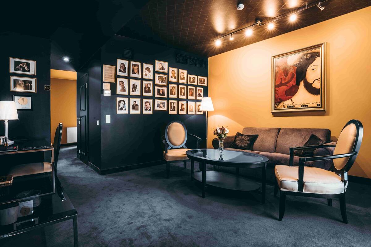 A modern lounge area with a dark wall adorned with framed photos, a round coffee table, a sofa, and a chair.