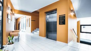 Een moderne hotelentree met een trap, lift en een zithoek.