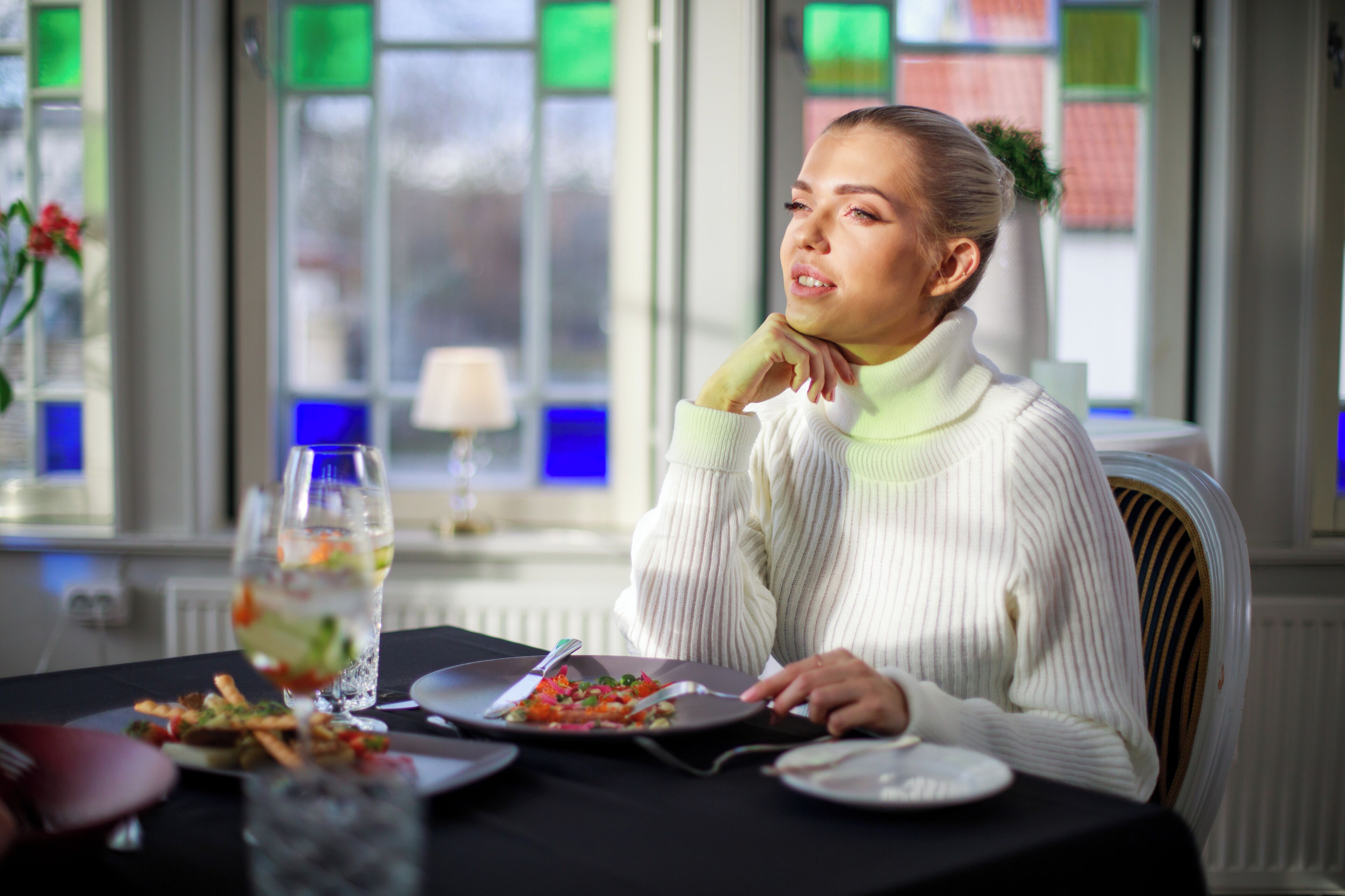 A person seated at a table with a plate of food, a glass of water, and a fork.