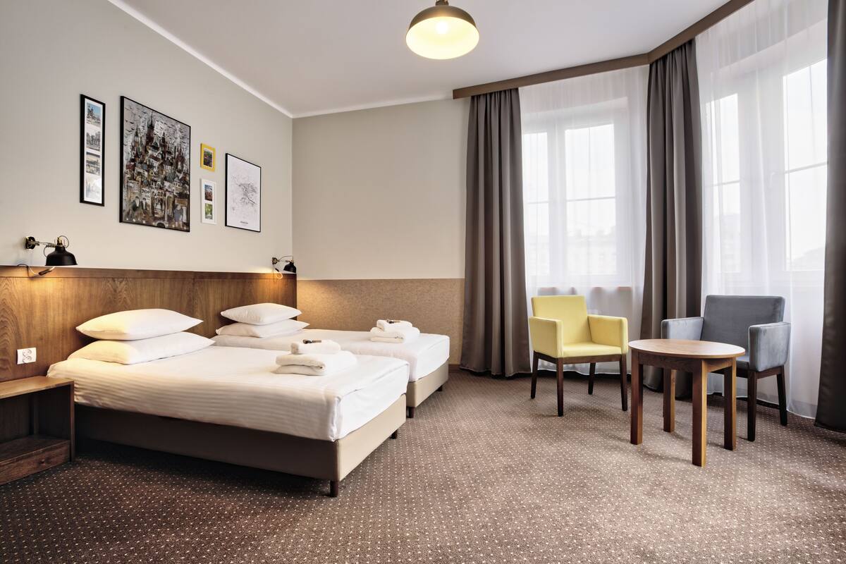 Hotelkamer met een groot bed, twee nachtkastjes, een kleine ronde tafel, twee stoelen en een groot raam met gordijnen.