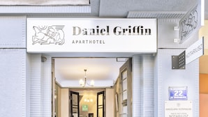 L’entrée de l’hôtel Daniel Griffin Apartment, avec son sol à motifs à carreaux, un panneau indicateur et un escalier menant à l’intérieur.