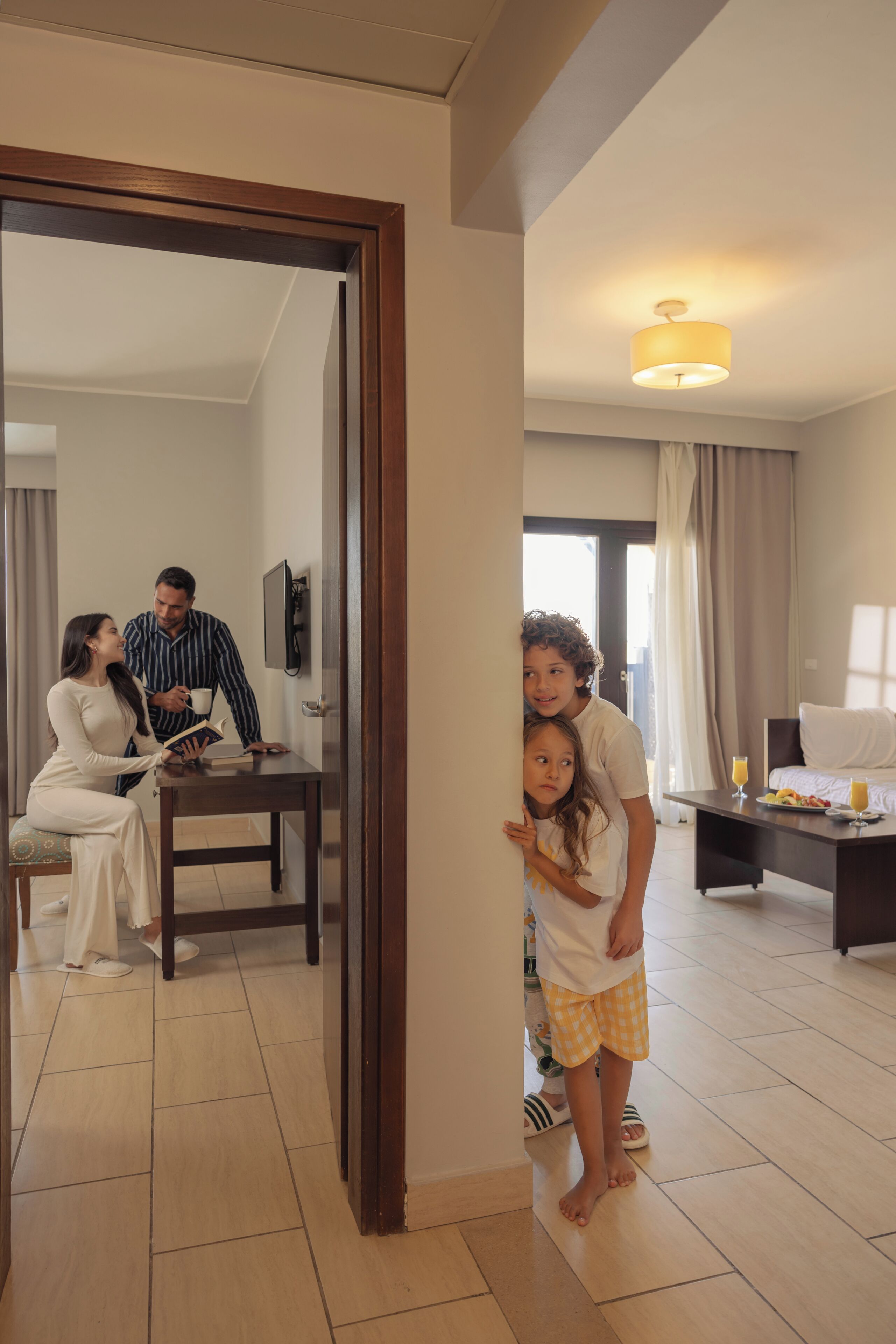 En familie i et moderne hotelværelse med spiseplads, seng og fjernsyn.